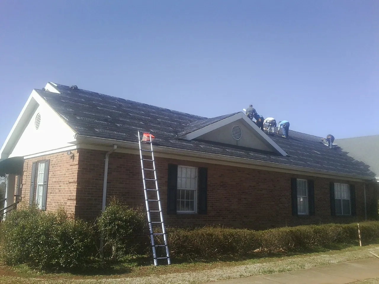 Crew tearing shingles off a brick ranch roof with a ladder set — Emergency Roof Repair work by our crew in West Mifflin