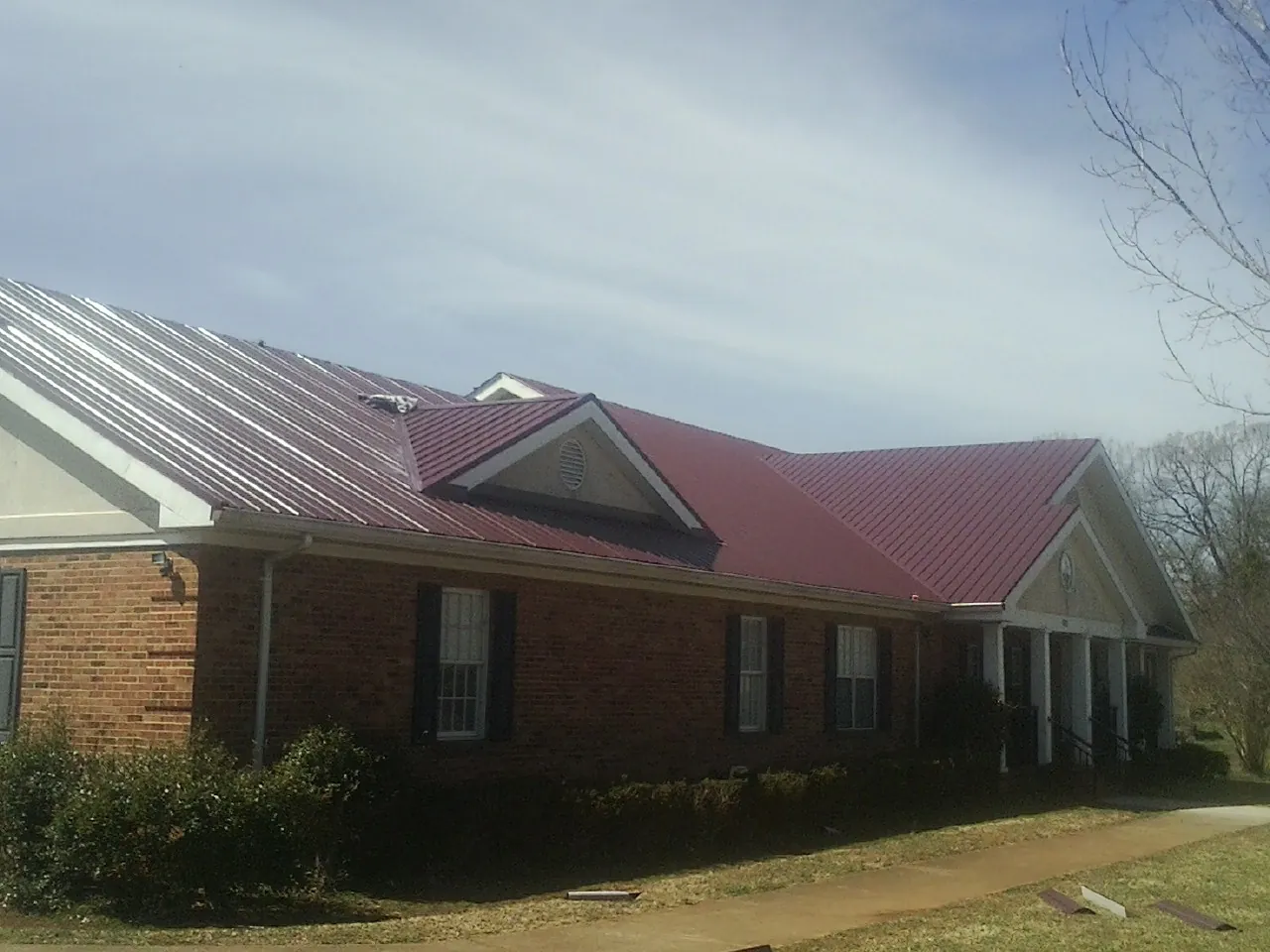 Red metal roof with gabled entries on a long brick building, from a Hail Damage Roof Repair job in West Mifflin