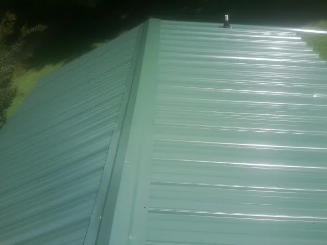 New green metal panels meeting at the ridge of a roof — Flat Roof Repair work by our crew in West Mifflin