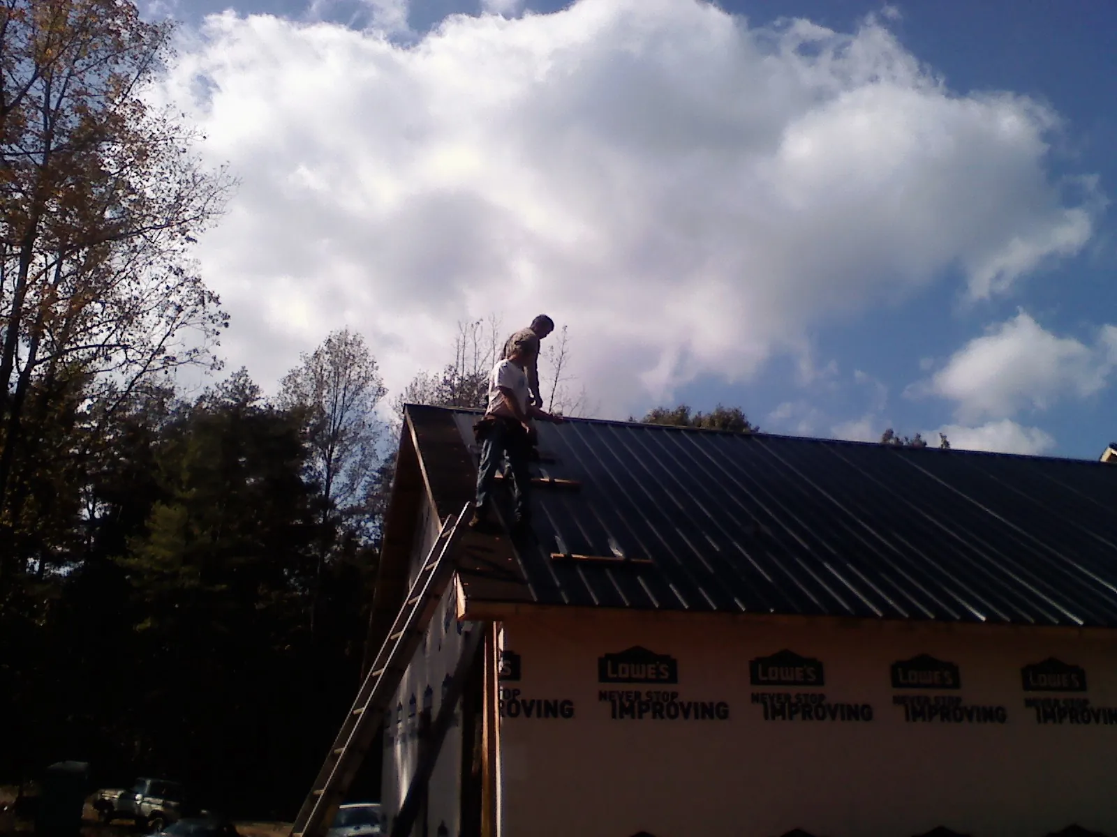 Roofer fastening dark metal panels high against a cloudy sky, from a Roof Inspection job in West Mifflin