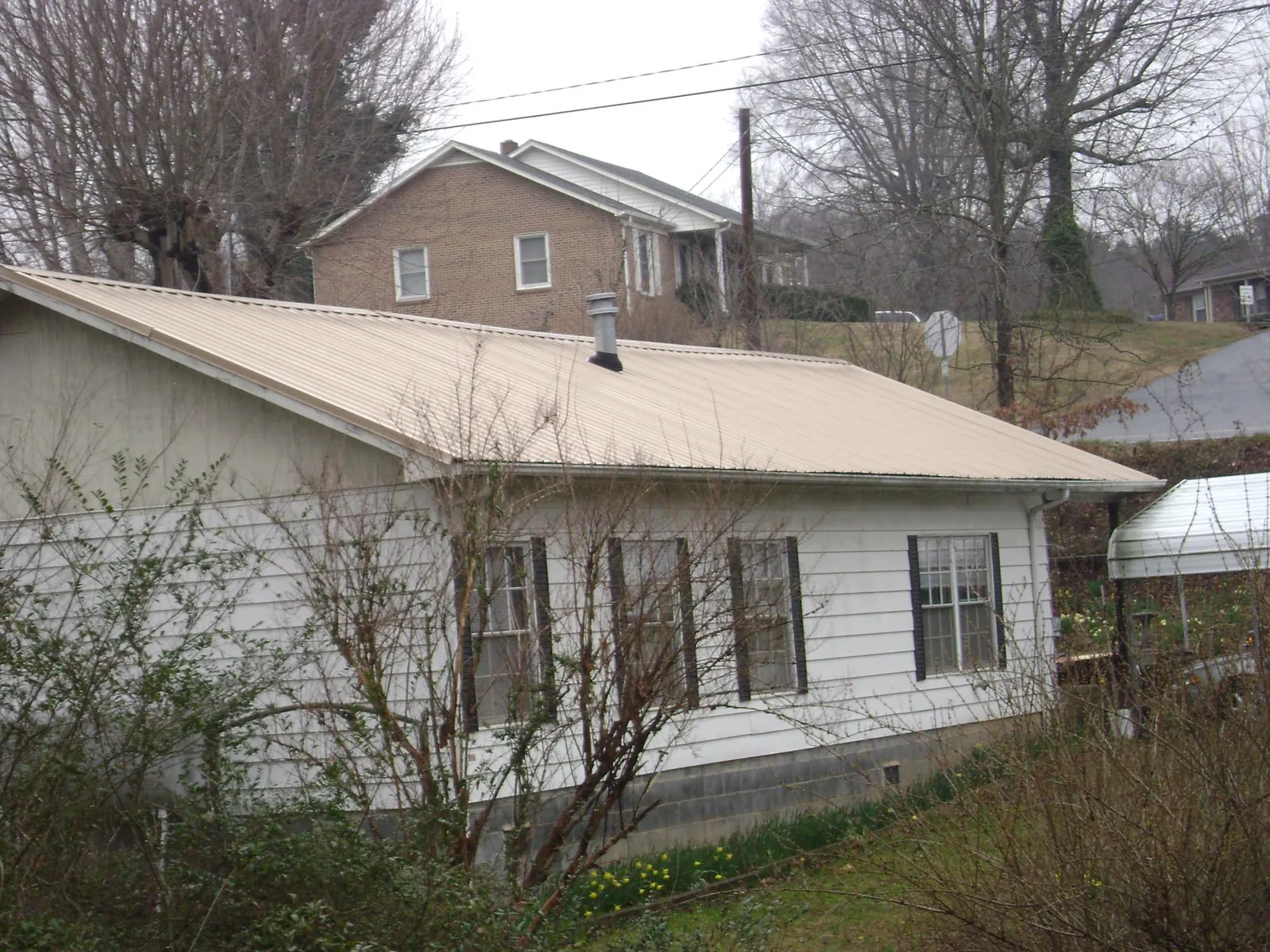 Tan metal roof on a white sided house set into a hillside — Commercial Roofing by Roofing Brothers in West Mifflin